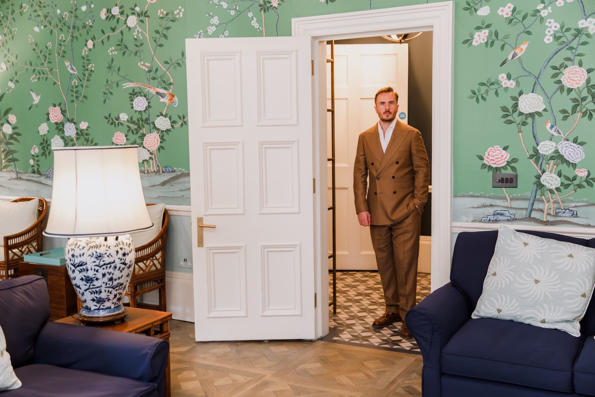 The waiting room: green botanical wallpaper, two navy sofas and a lamp, with Dr Ben Davis standing in the open doorway