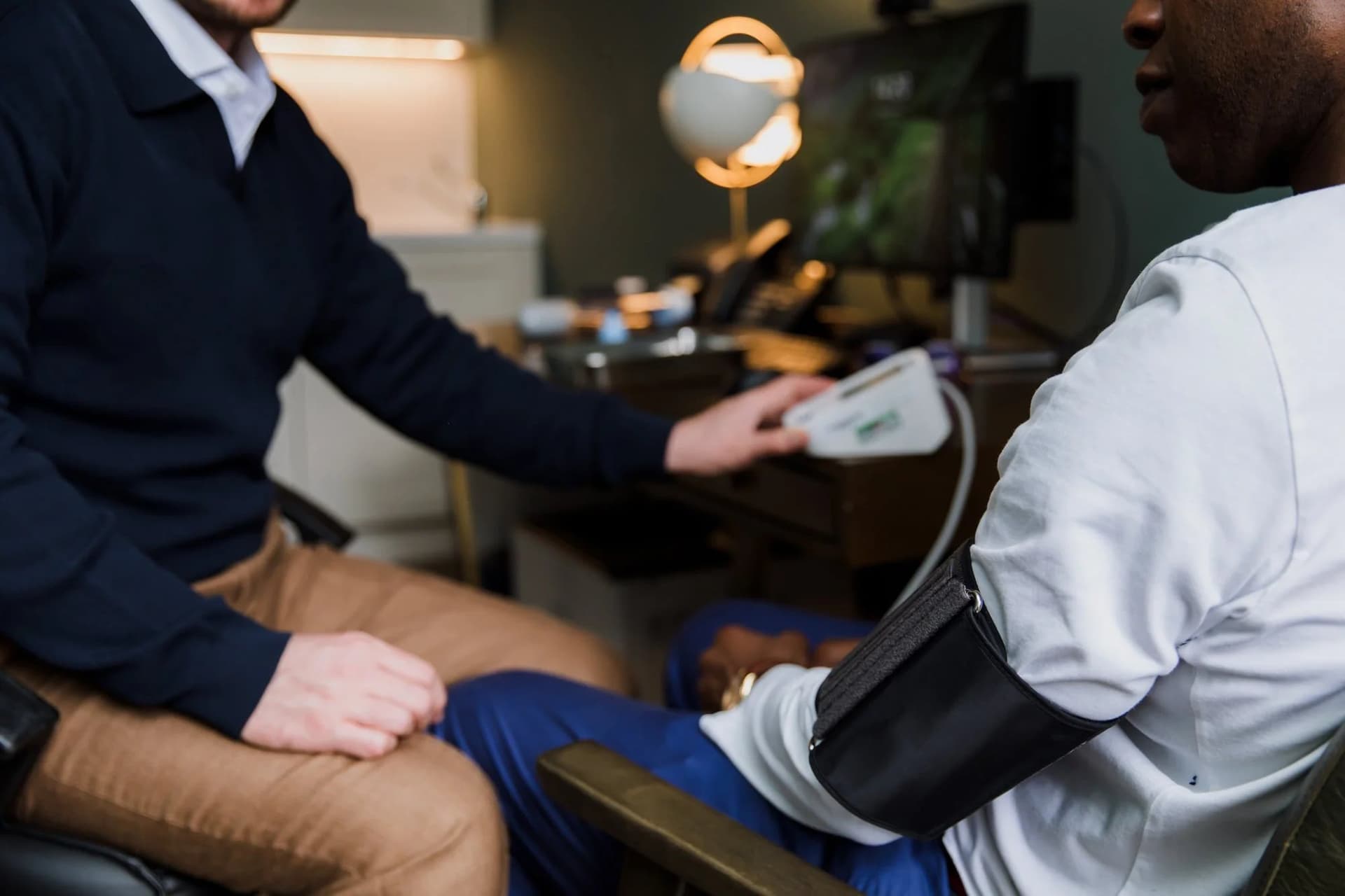 A blood pressure cuff being fitted to a patient’s upper arm at the consulting room desk, neither face in frame