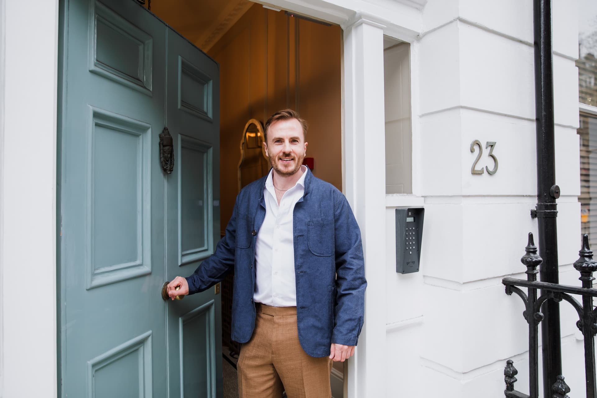 Dr Ben Davis holding open the green front door of number 23 Devonshire Place, a white stucco townhouse
