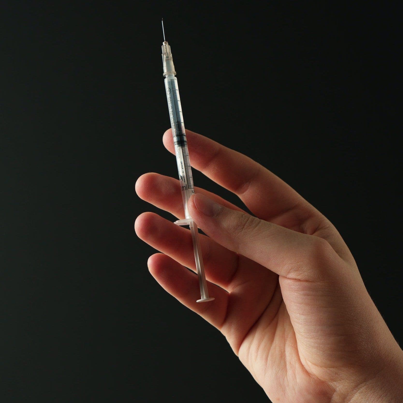 A hand holding a small syringe upright against a dark background.