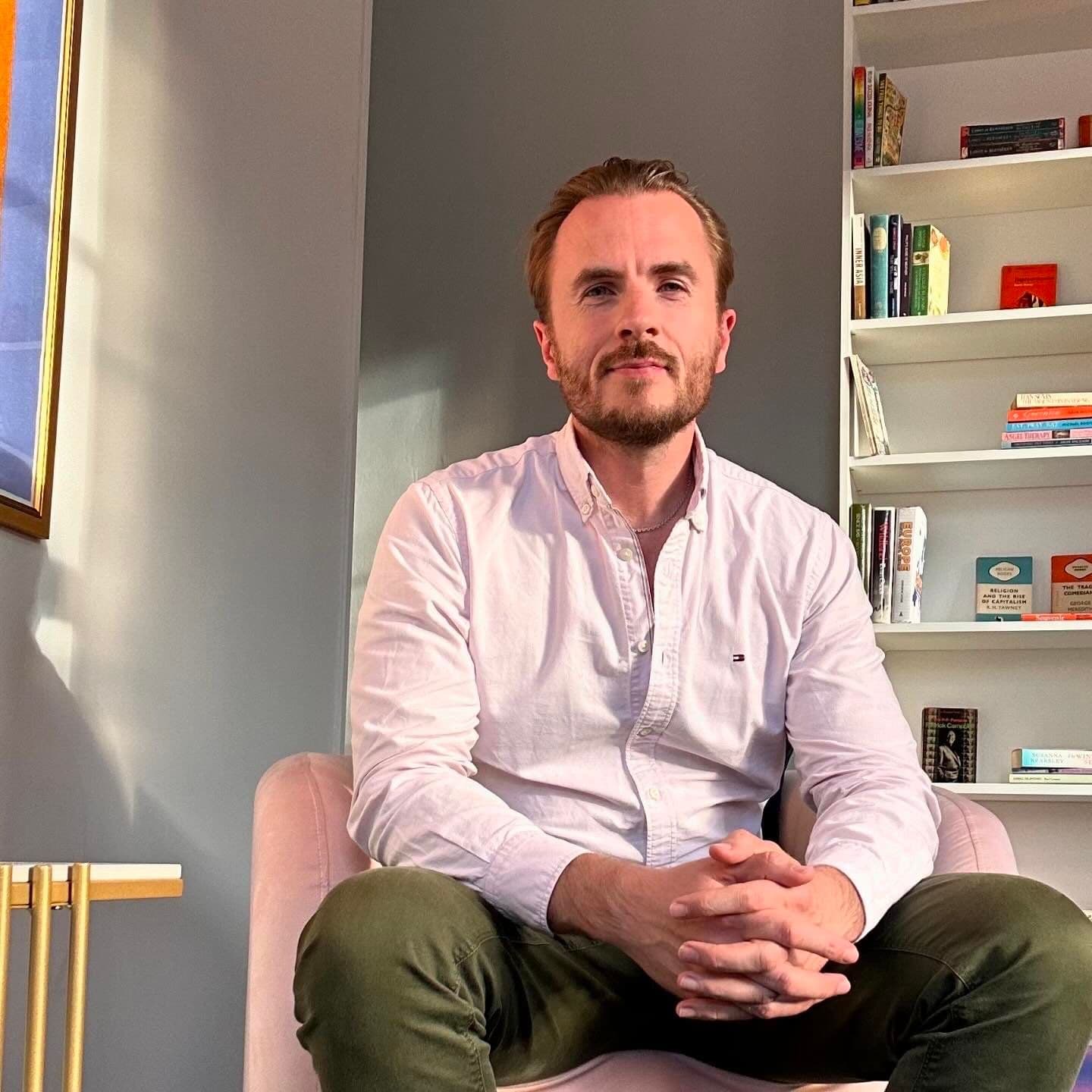 Dr Ben Davis sitting in an armchair in his consulting room, hands loosely clasped, bookshelves behind him.